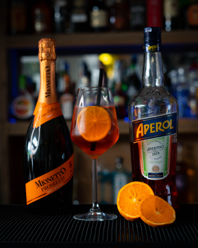 The Aperol Spritz on a bar countertop, surrounded by its ingredients