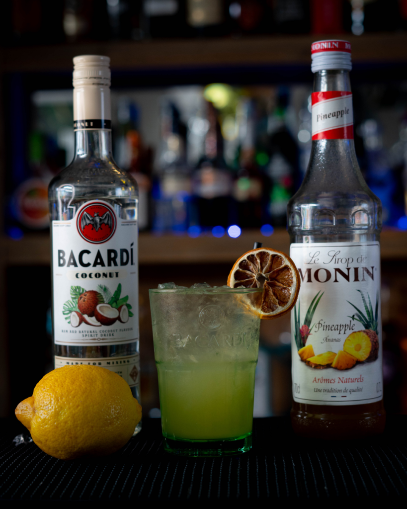 The Coco Colada Spritz on a bar top, surrounded by its ingredients.