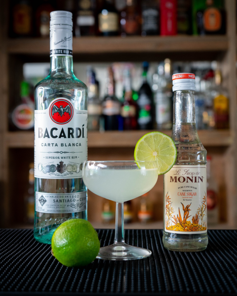 The Daiquiri on a bar countertop, surrounded by its ingredients