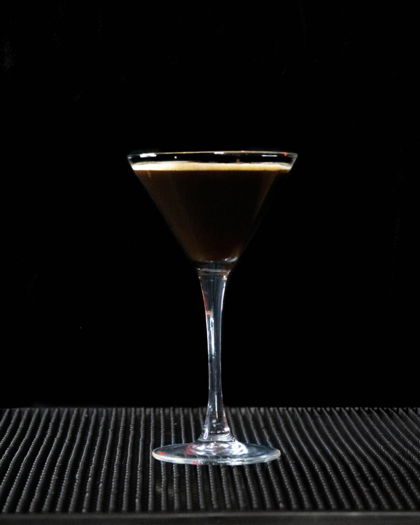 The Espresso Martini on a bar countertop with a black background