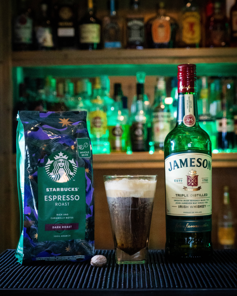 Irish Coffee on a bartop, surrounded by its ingredients.