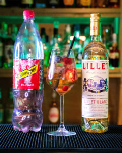 The Wildberry Lillet on a bar top, surrounded but its ingredients