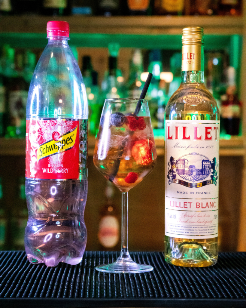 The Wildberry Lillet on a bar top, surrounded but its ingredients