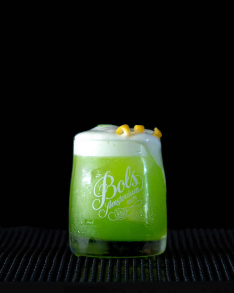 The Melon Sour on a bar top with a black background.