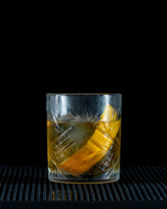 The Old Fashioned cocktail on a home bartop with a black background.