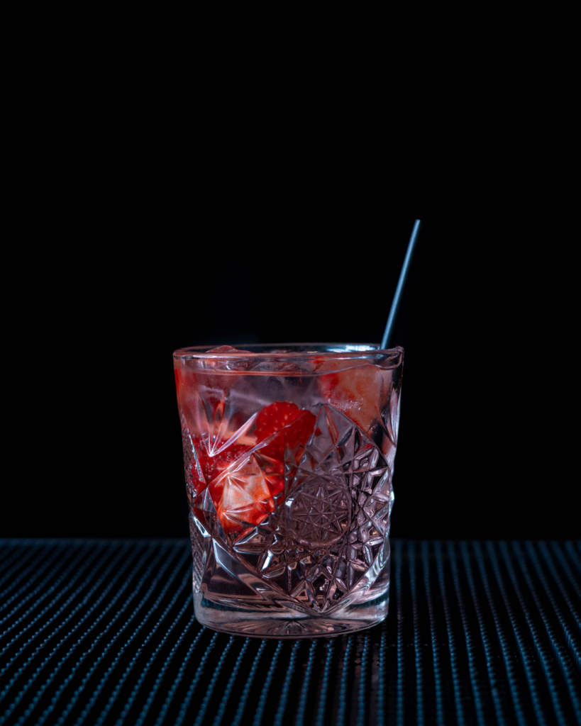 The Pink Gin Rose Lemonade on a bar countertop with a black background