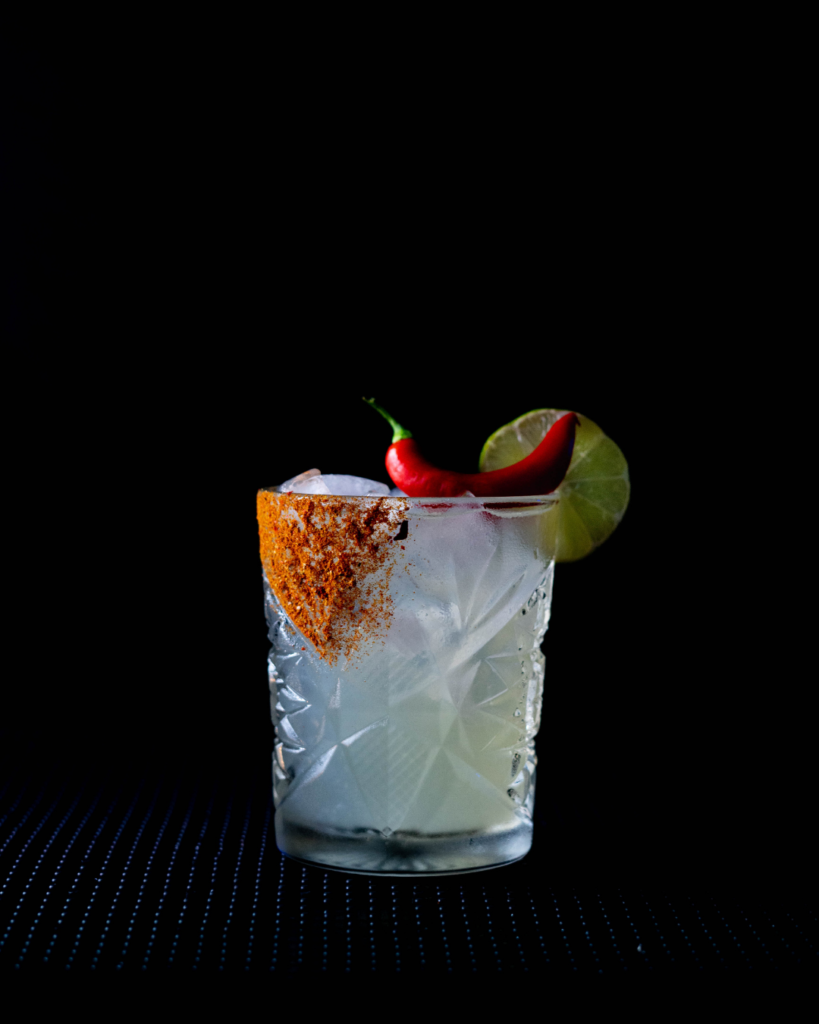 The Red Chili Margarita on a bar countertop with a black background.