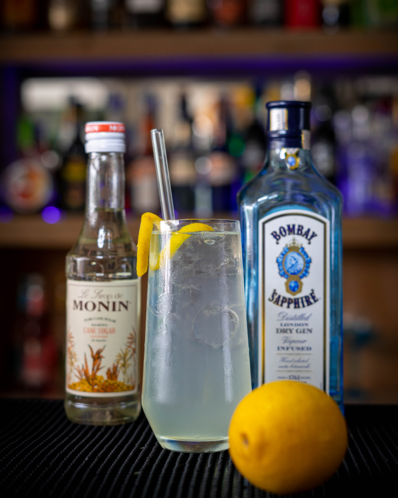 The Tom Collins on a bar countertop, surrounded by its ingredients