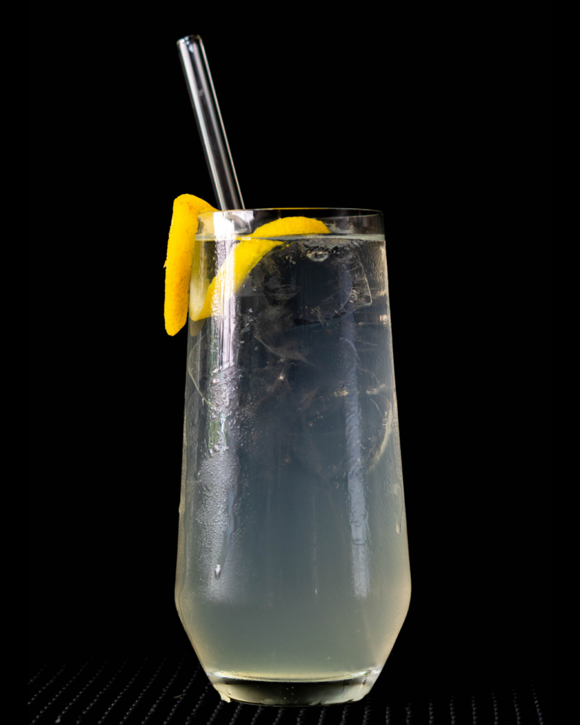 The Tom Collins on a bar countertop with a black background