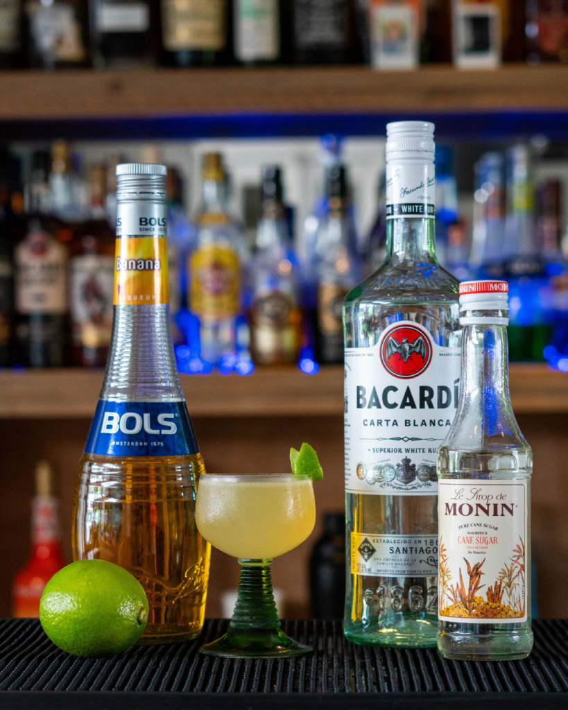 The Banana Daiquiri on a bartop, surrounded by its ingredients