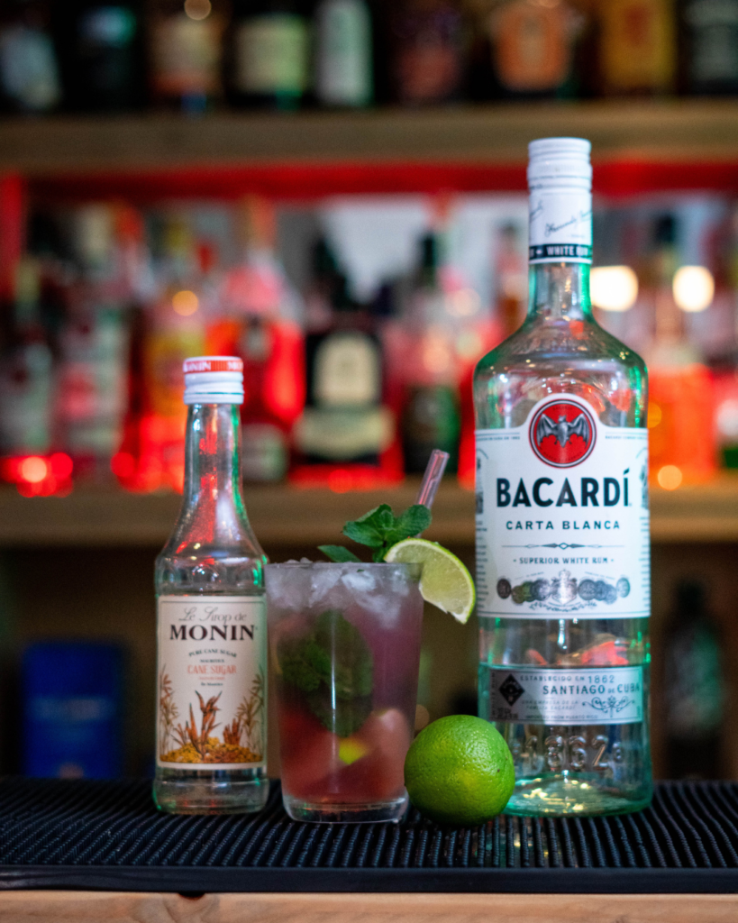 The Cranberry Mojito on a bartop, surrounded by its ingredients