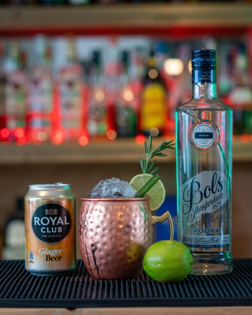 The Cranberry Mule on a bartop, surrounded by its ingredients.