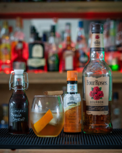 The Gingerbread Old Fashioned, surrounded by its ingredients on a home bar top