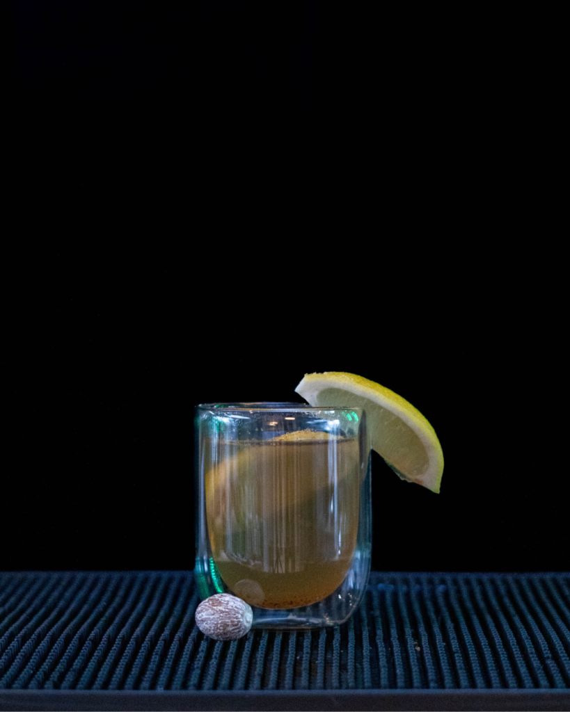 The Nutmeg Hot Toddy on a bar top with a black background