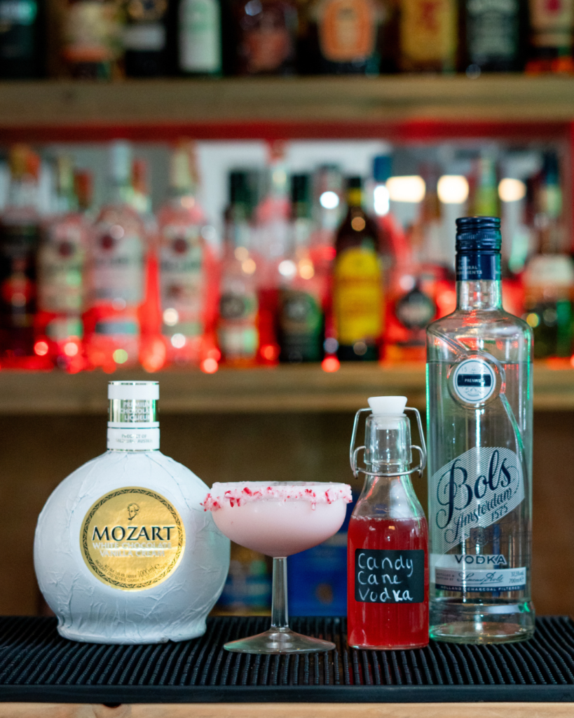 The Candy Cane Martini on a bar top, surrounded by its ingredients.