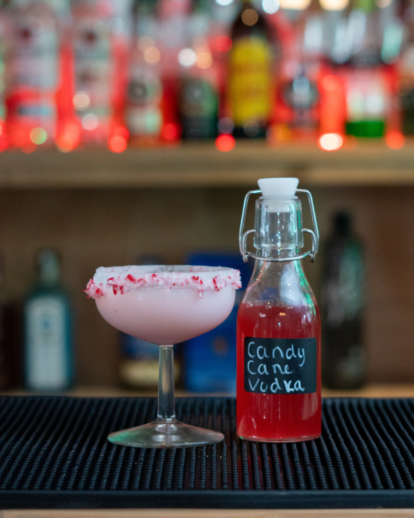 The Candy Cane Martini and a small bottle of candy cane infused vodka on a bar top.