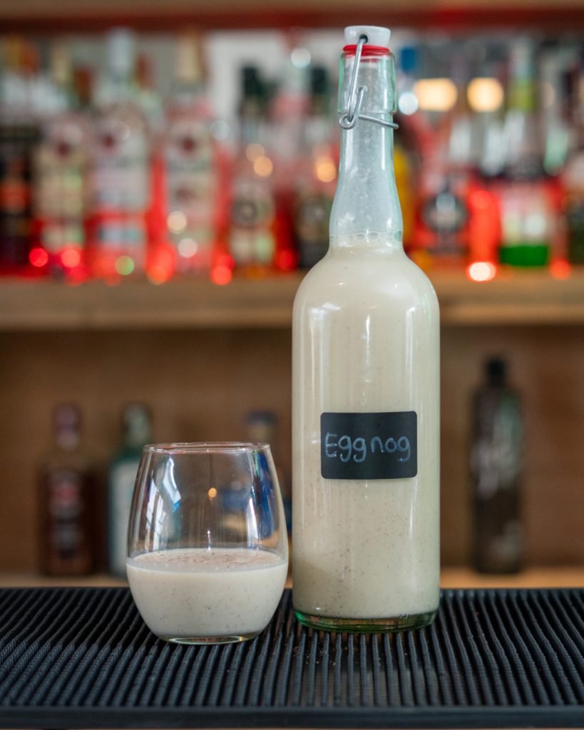 A bottle and a glass of eggnog on a bar top