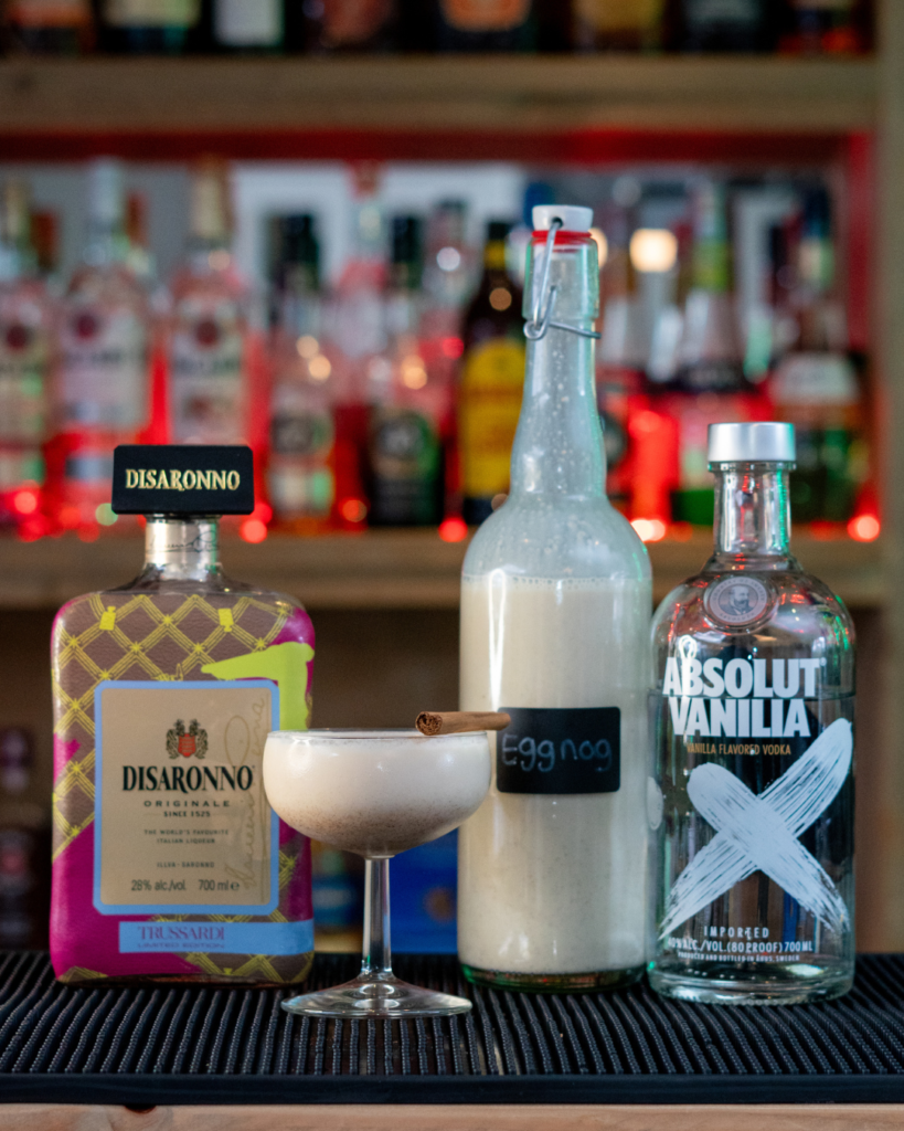 The Eggnog Martini on a bar top, surrounded by its ingredients.