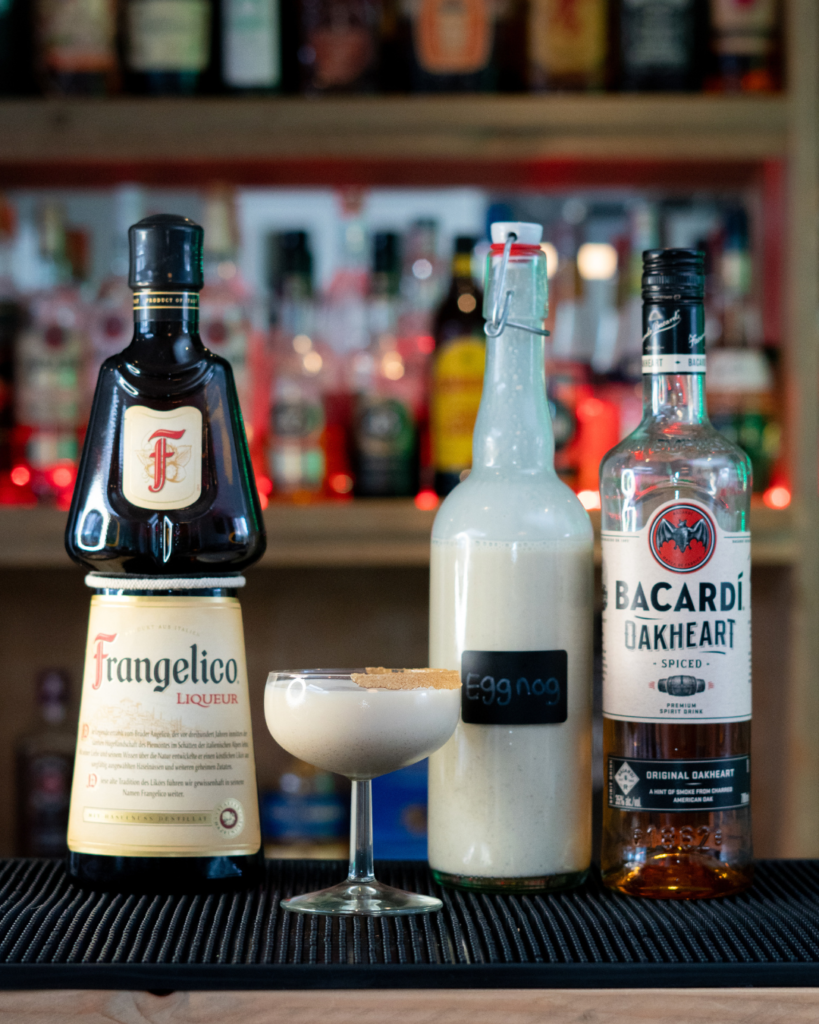 The Spiced Eggnog Martini on a bar top, surrounded by its ingredients.