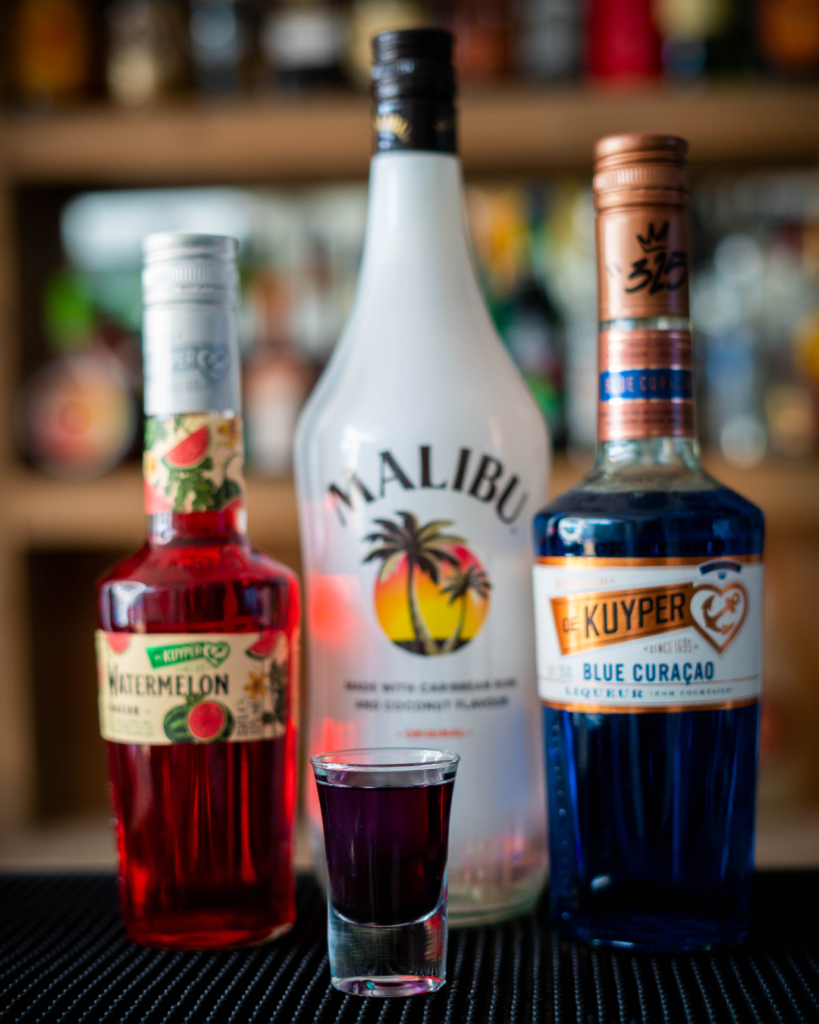 The Purple or Tropical Mystery Shot on a bar top, surrounded by its ingredients.