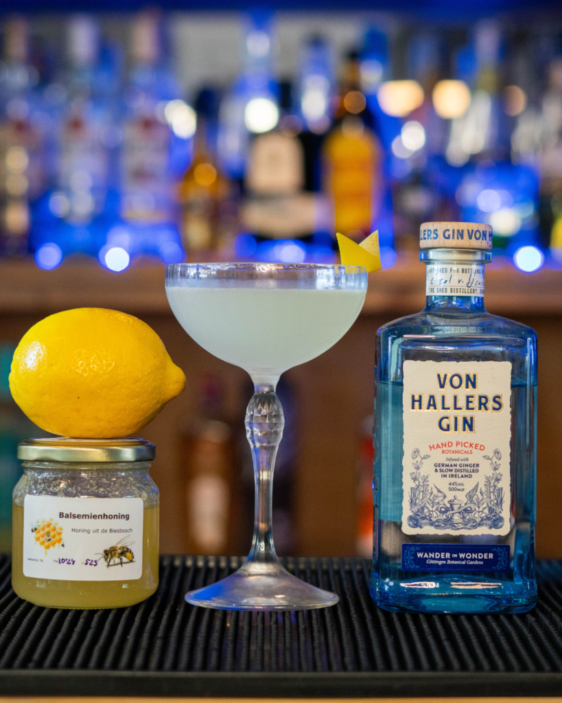 The Bees Knees on a bar top, surrounded with its ingredients.