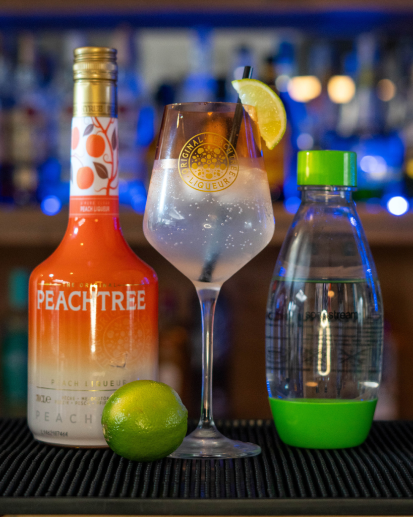 The Fizzy Peachtree on a bartop, surrounded by its ingredients.