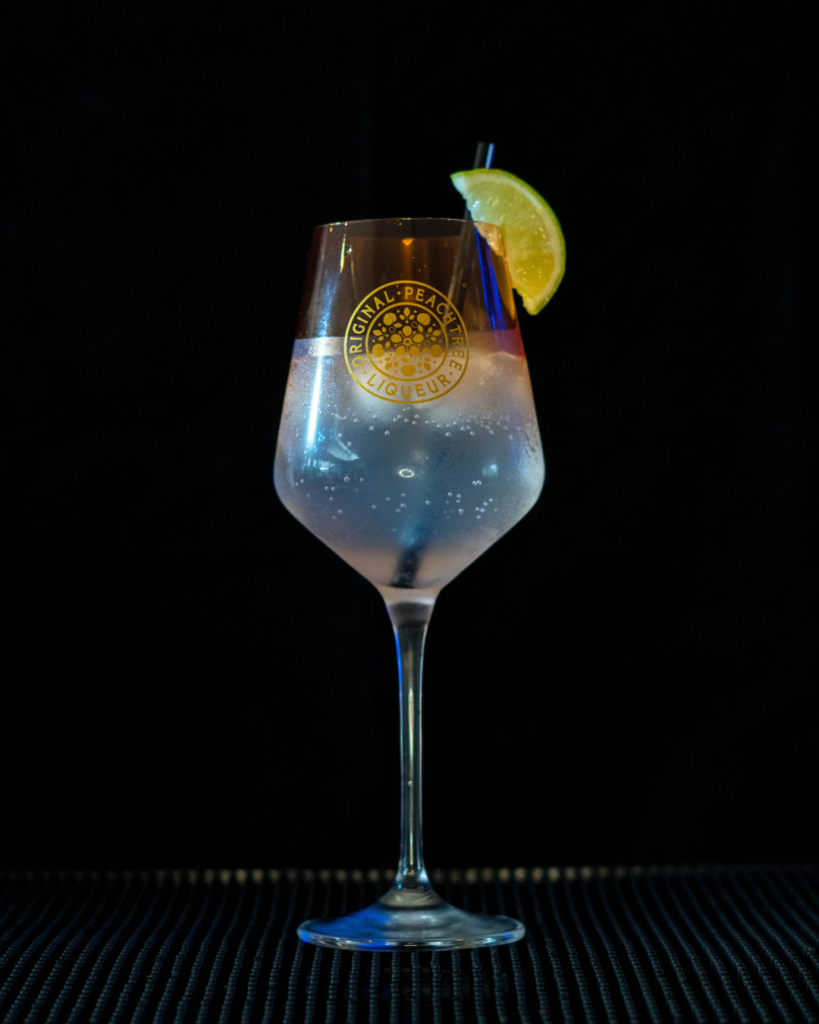 The Fizzy Peachtree on a bartop with a black background.