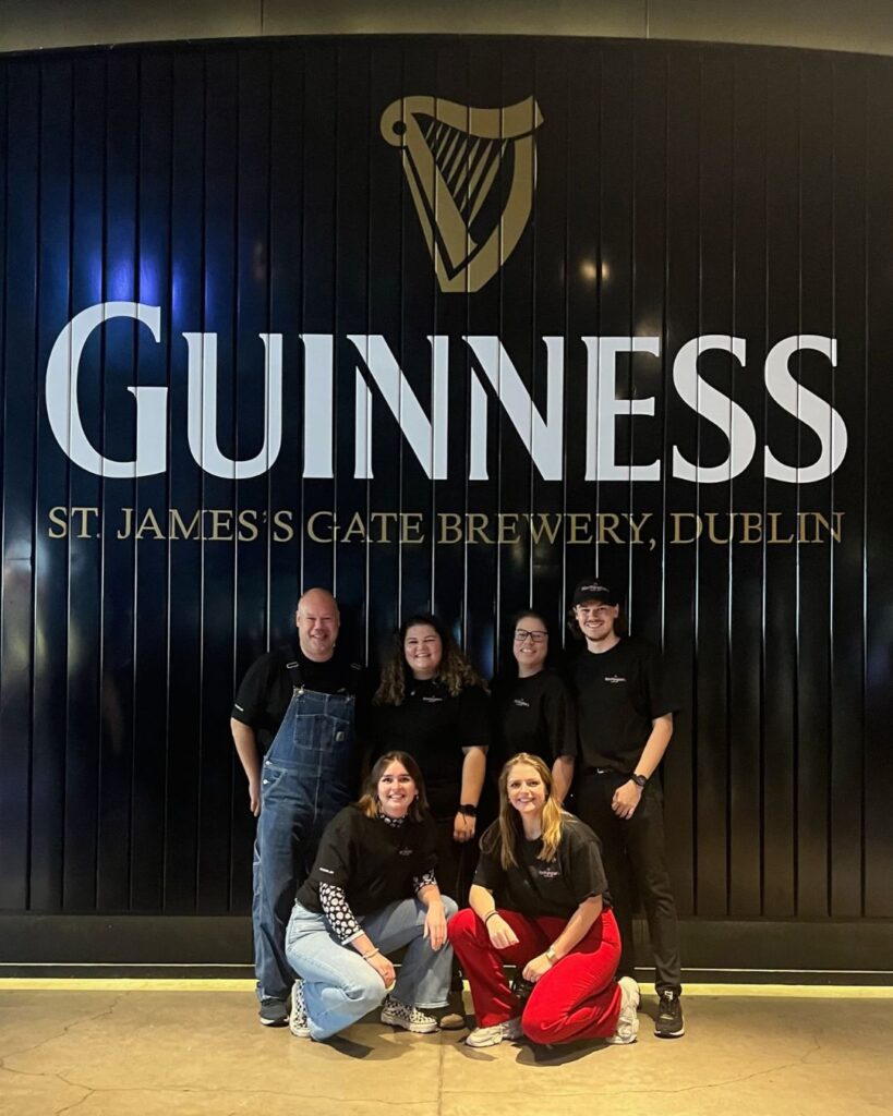 Edward, Joy, Elize, Xander, Britt & Cathelijn in front of a black door with the Guinness logo.