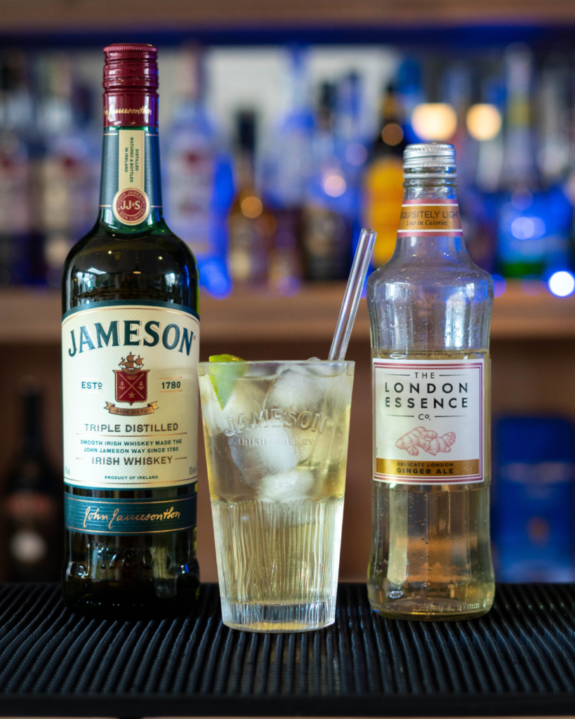 The Jameson Ginger & Lime (JGL) cocktail on a bartop, surrounded by its ingredients.