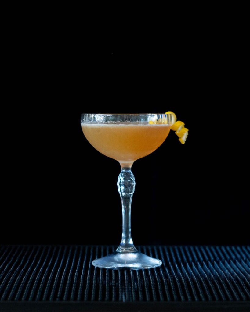 The Sidecar cocktail on a bartop with a black background.