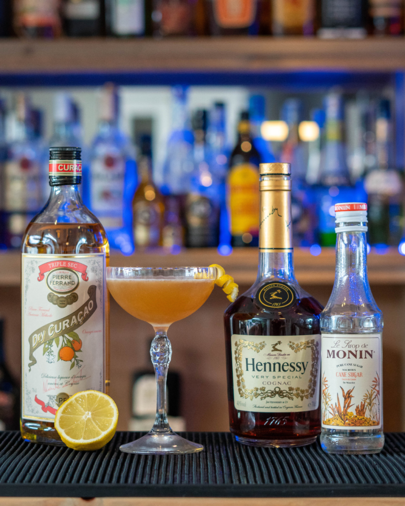 The Sidecar cocktail on a bartop, surrounded by its ingredients.