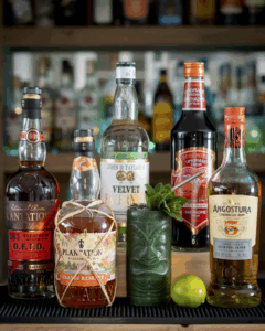 The zombie Cocktail in a green tiki glass surrounded by its ingredients on a home bartop.