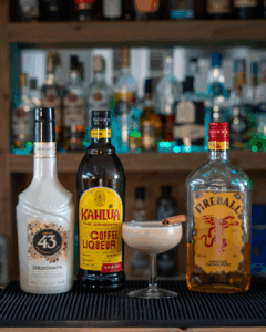 The Cinnamon Roll Martini on a home bartop surrounded by its ingredients.