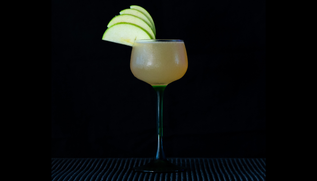 The Appletini on a home bartop with a black background.