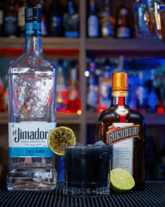 The Black Margarita on a home bartop, surrounded by its ingredients.