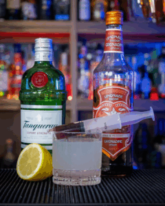 The Bloody Gin Fizz Halloween Cocktail on a home bartop surrounded by its ingredients.