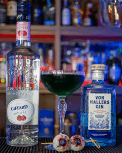 The Eye See You Halloween cocktail on a home bartop surrounded by its ingredients.