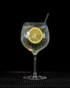 Gin & Tonic: Gordon's London Dry Gin & Schweppes Indian Tonic mixed on a home bartop with a black background..
