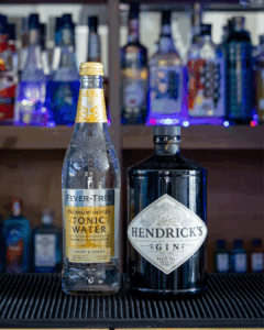 Hendricks Gin Bottle and a bottle of Fever-tree Indian Tonic Water on a home bartop with a black background.
