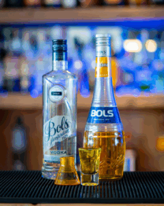 The Boo-zy Lab Kit, Halloween shots; the yellow shot. The shots on a home bartop, surrounded by its ingredients.