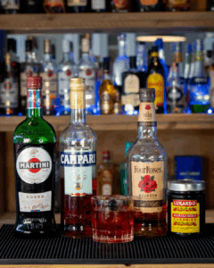 the Boulevardier cocktail on a home bartop surrounded by its ingredients.