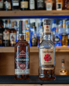 A bottle of Rye Whiskey, Rittenhouse and a bottle of Bourbon, Four Roses on a home bar top.