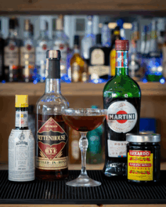 the Manhattan cocktail on a home bartop surrounded by its ingredients.