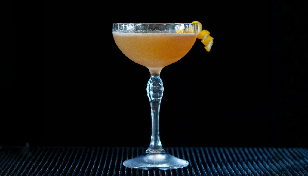 The Sidecar cocktail on a bartop with a black background.