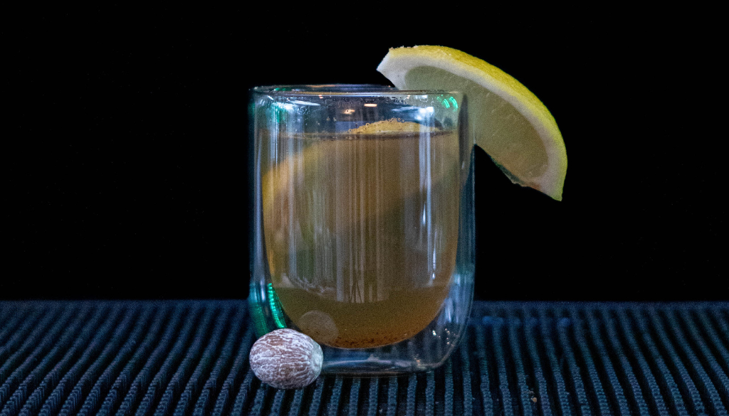 The Nutmeg Hot Toddy on a bar top with a black background