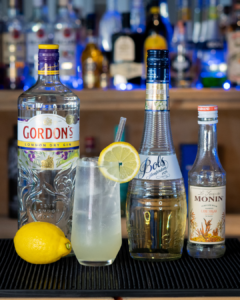 The Elderflower Collins on a home bar top surrounded by its ingredients