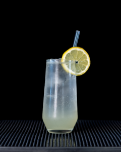 The Elderflower Collins on a home bar top with an all black background