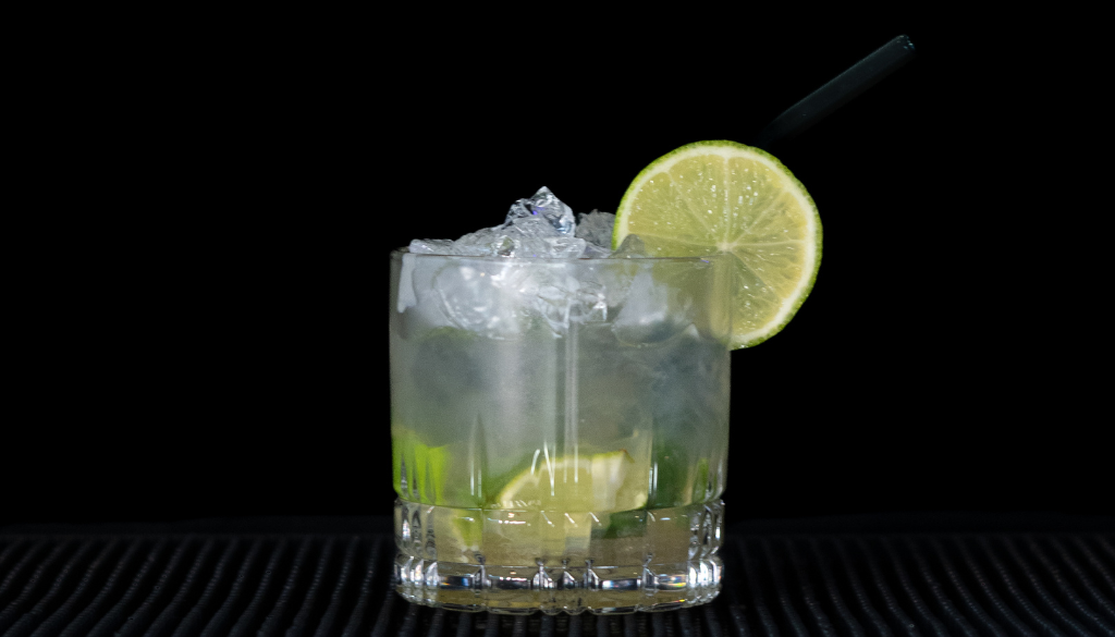 The caipiroska cocktail on a home bar top with an all black background.