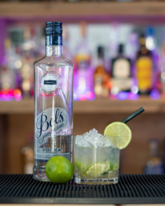 The caipiroska cocktail on a home bar top, surrounded by its ingredients.