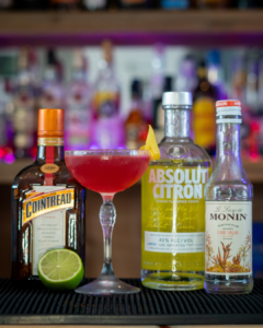The Cosmopolitan cocktail on a home bar top surrounded by its ingredients